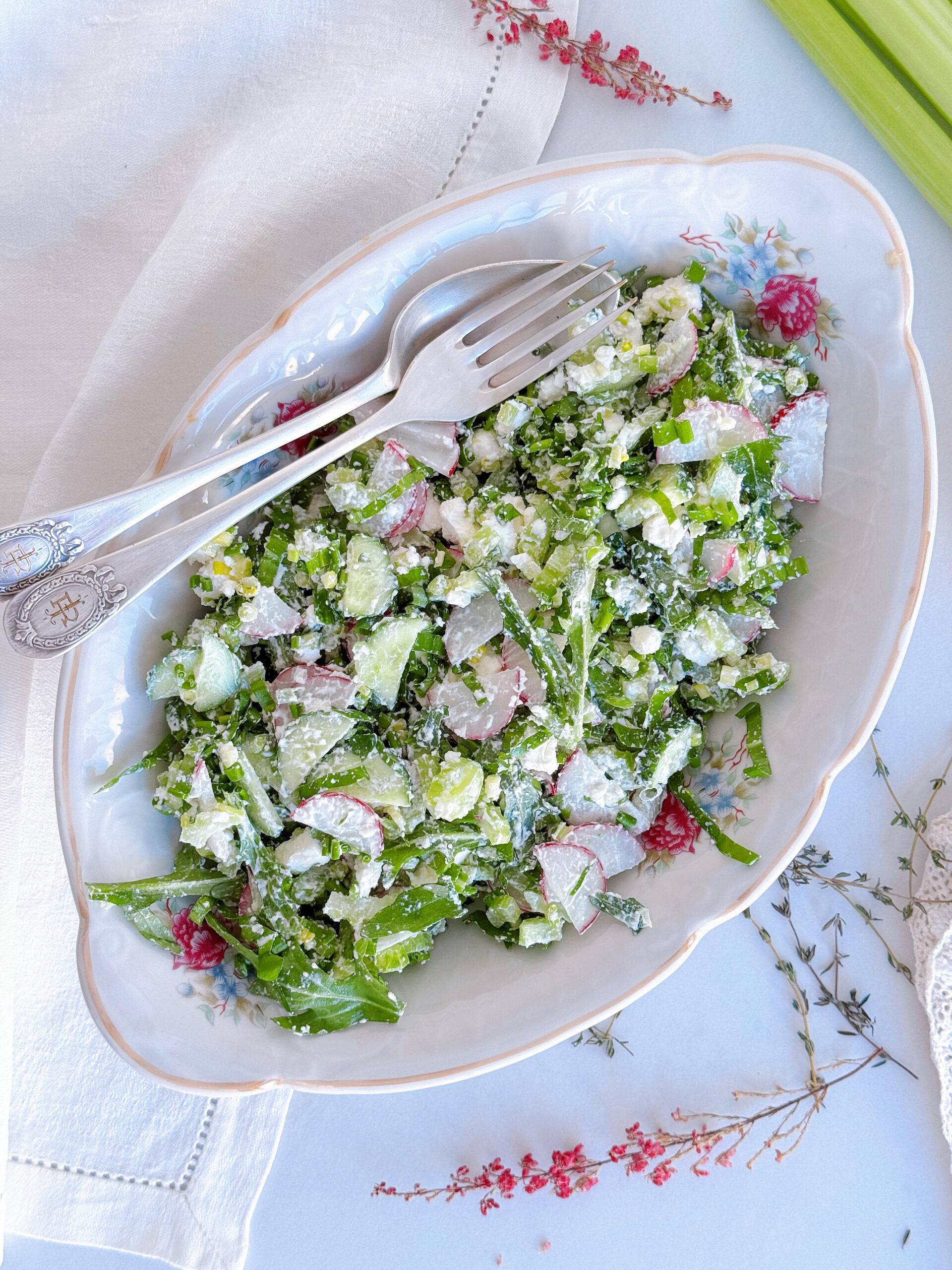 зелений салаз з молодих весняних овочів поданий на тарілці з квітами і срібним. посудом