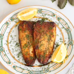 Скумбрія запечена в духовці з хрумкою скоринкою. Подається з лимоном та зеленню на порцеляновій тарілці