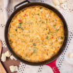 Керамічна форма із запеченим золотистим гратеном з гарбуза та цвітної капусти, прикрашеним хрусткими зеленими листочками шавлії на фоні лляної серветки.