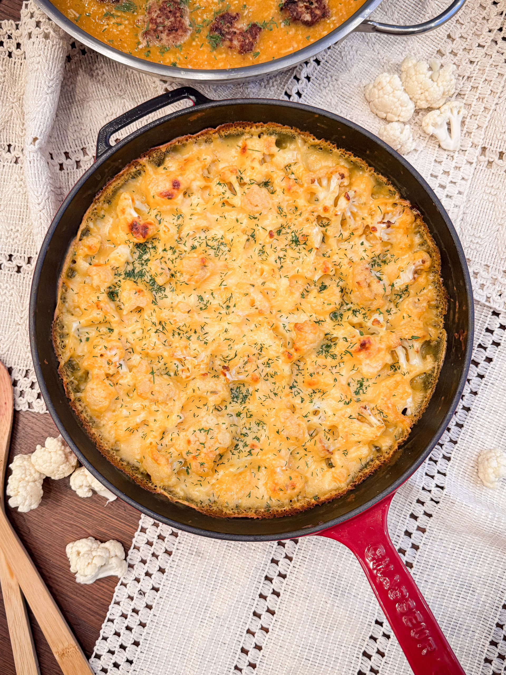 Керамічна форма із запеченим золотистим гратеном з гарбуза та цвітної капусти, прикрашеним хрусткими зеленими листочками шавлії на фоні лляної серветки.