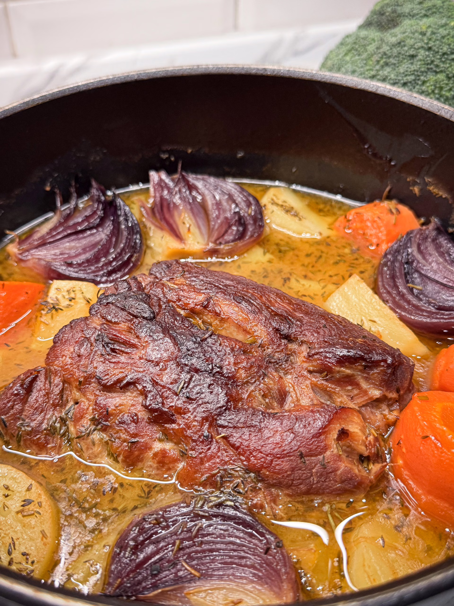 Цілий шматок томленого свинячого ошийка в густому соусі з великими шматками запеченої картоплі та моркви, поданий у керамічній тарілці та прикрашений гілочками свіжого чебрецю.