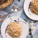 тарілка з тушкованою капустою у кремовому сирному соусі качо-е-пепе з вкрапленнями чорного перцю, подана на матовій кераміці у стилі мінімалізму.