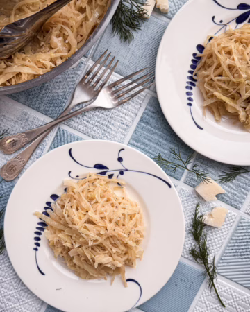 тарілка з тушкованою капустою у кремовому сирному соусі качо-е-пепе з вкрапленнями чорного перцю, подана на матовій кераміці у стилі мінімалізму.