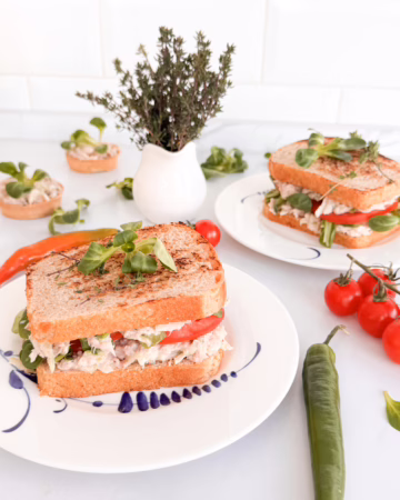 Апетитний клаб-сендвіч з тунцем, грушею та свіжим томатом на тарілці.