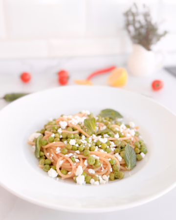 Тарілка апетитної пасти спагеті з яскравим зеленим горошком, цедрою лимона та пластівцями чилі, сервірована з кисломолочним сиром.