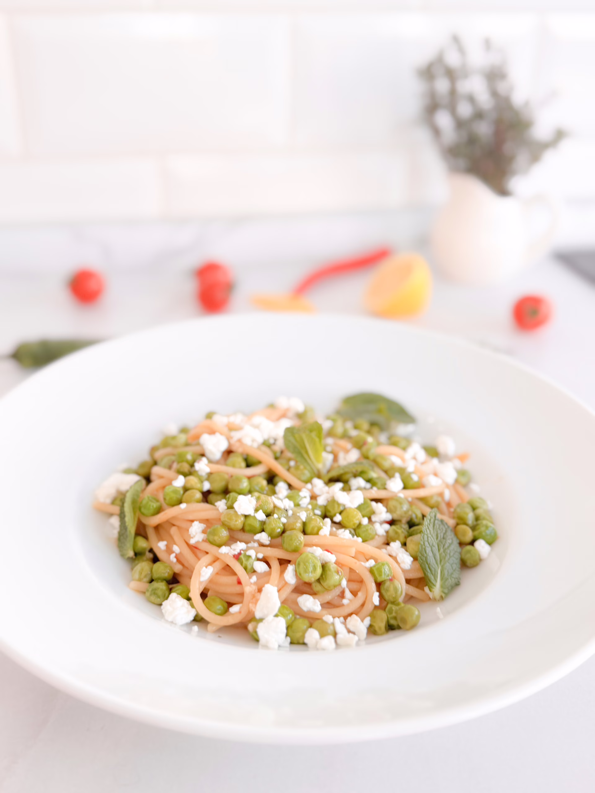 Тарілка апетитної пасти спагеті з яскравим зеленим горошком, цедрою лимона та пластівцями чилі, сервірована з кисломолочним сиром.