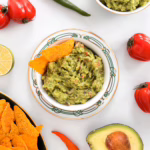 Свіжий домашній гуакамоле в керамічній мисці, поданий з кукурудзяними чипсами начос та шматочками лайма на столі.