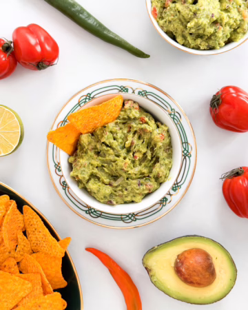 Свіжий домашній гуакамоле в керамічній мисці, поданий з кукурудзяними чипсами начос та шматочками лайма на столі.