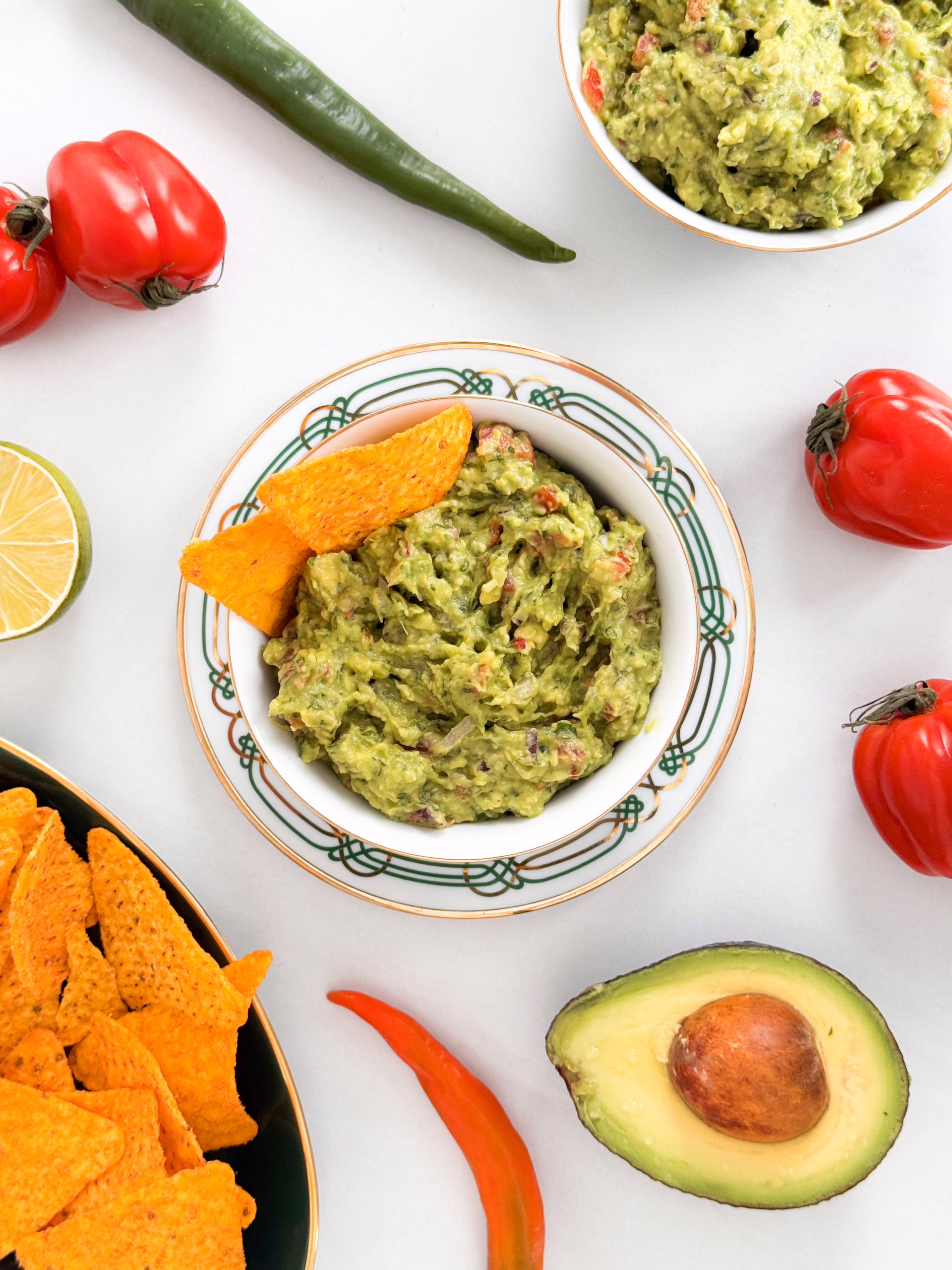 Свіжий домашній гуакамоле в керамічній мисці, поданий з кукурудзяними чипсами начос та шматочками лайма на столі.