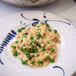 Порція кремового перлового кускусу з хрустким беконом та зеленим горошком, подана у вінтажній тарілці заводу Villeroy & Boch, прикрашена тертим пармезаном.