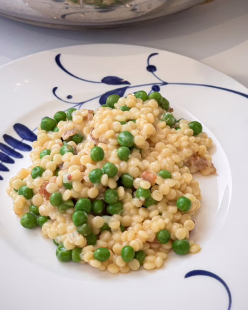 Порція кремового перлового кускусу з хрустким беконом та зеленим горошком, подана у вінтажній тарілці заводу Villeroy & Boch, прикрашена тертим пармезаном.