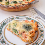 Шматочок апетитного кіша з лососем та броколі на ніжній морквяній основі, поданий на світлій керамічній тарілці ручної роботи.