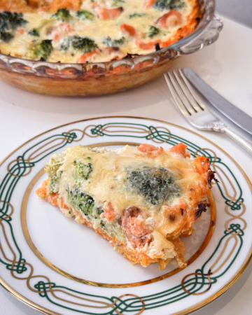 Шматочок апетитного кіша з лососем та броколі на ніжній морквяній основі, поданий на світлій керамічній тарілці ручної роботи.