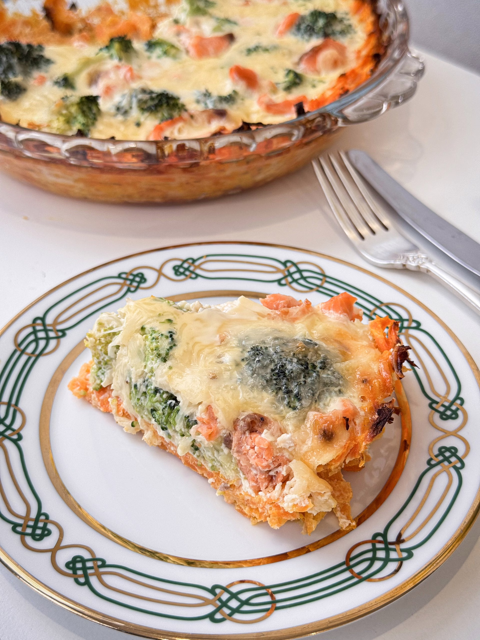 Шматочок апетитного кіша з лососем та броколі на ніжній морквяній основі, поданий на світлій керамічній тарілці ручної роботи.