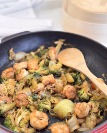 Апетитна порція овочів (зелена броколі, пак-чой, пекінська капуста) зі смаженими креветками в соєво-місо соусі, прикрашена свіжою кінзою на красивій керамічній