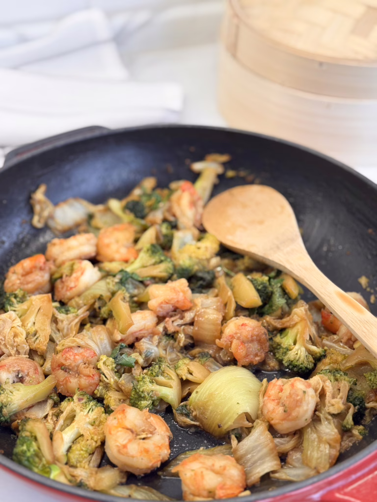 Апетитна порція овочів (зелена броколі, пак-чой, пекінська капуста) зі смаженими креветками в соєво-місо соусі, прикрашена свіжою кінзою на красивій керамічній