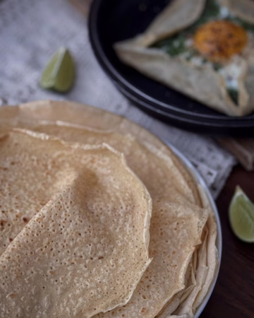 Апетитний бретонський креп із зеленої гречки, загорнутий конвертом на тарілці, з начинкою із розплавленого сиру, шпинату та томатів.