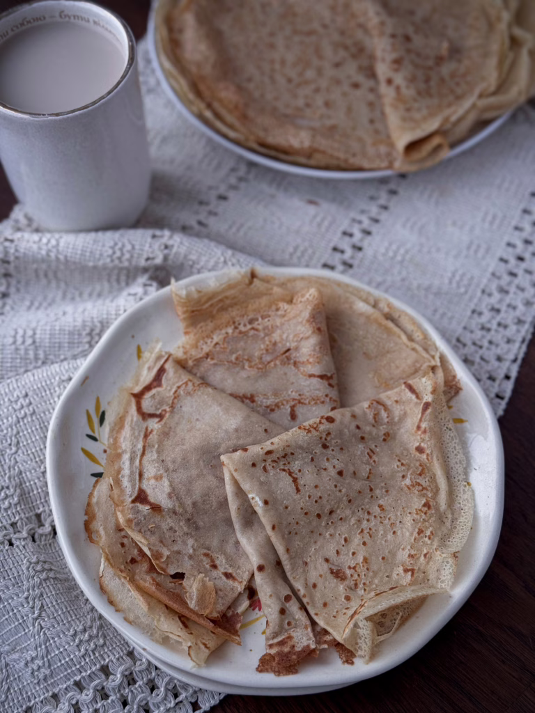 Тонкі, еластичні млинці з борошна зеленої гречки, апетитно згорнуті на тарілці, з золотистою скоринкою.