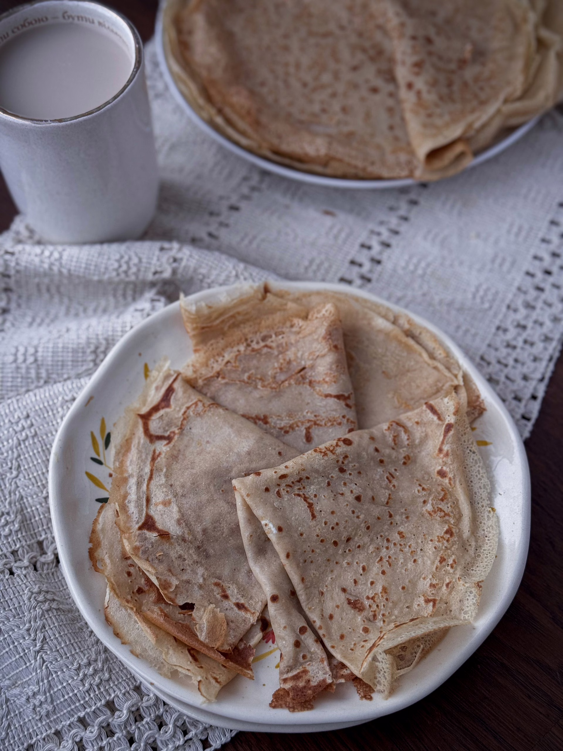 Тонкі, еластичні млинці з борошна зеленої гречки, апетитно згорнуті на тарілці, з золотистою скоринкою.