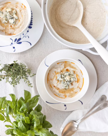 Сервірування гарячого крем-супу з цвітної капусти у білій керамічній піалі Villeroy & Boch з блакитним розписом, прикрашеного сиром з пліснявою та гострою олією, CookItTwice стиль.