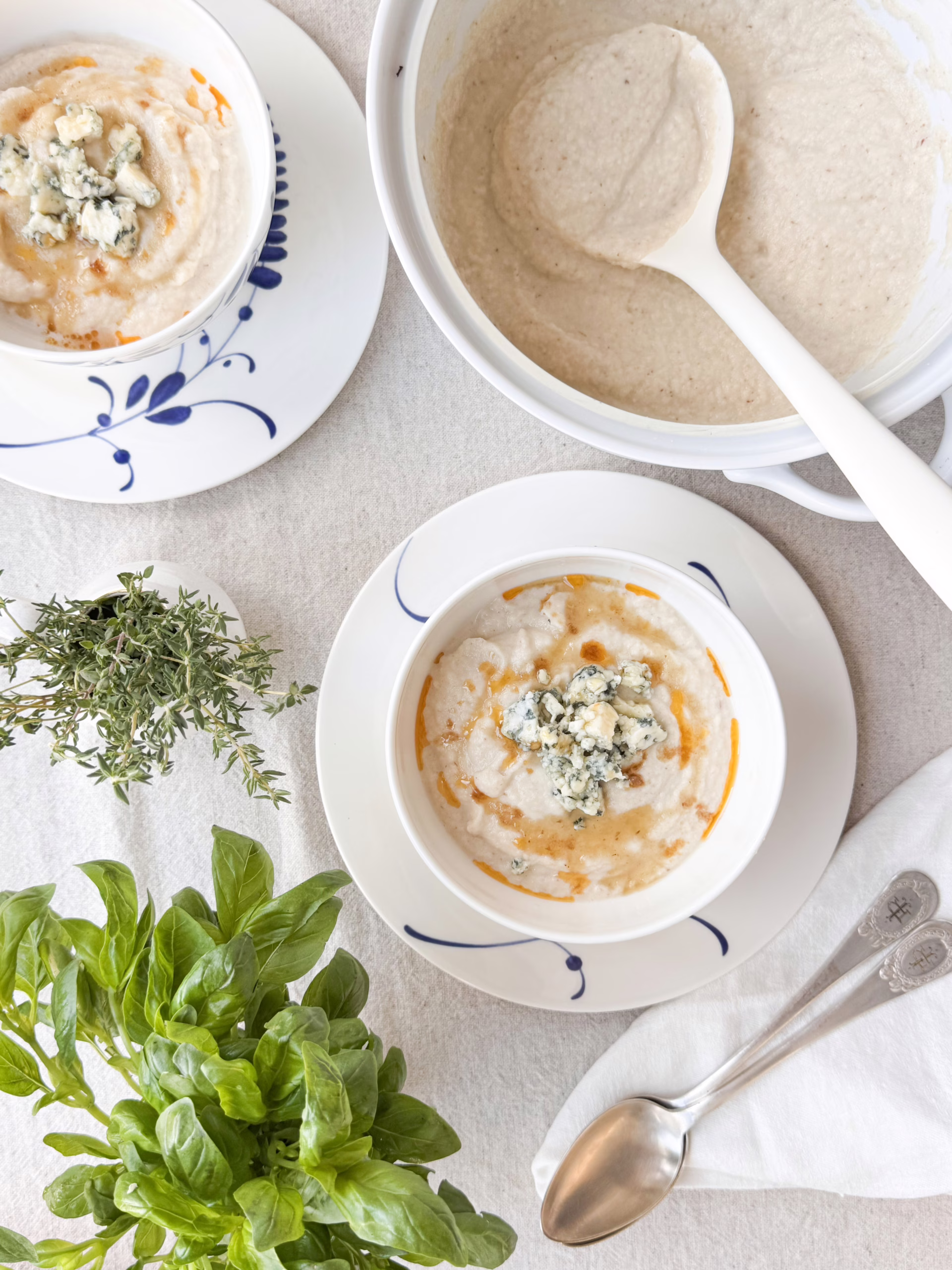 Сервірування гарячого крем-супу з цвітної капусти у білій керамічній піалі Villeroy & Boch з блакитним розписом, прикрашеного сиром з пліснявою та гострою олією, CookItTwice стиль.