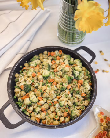 різнокольорова паста з зеленими овочами подана на чавунній пательні