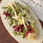 ервірування хрусткого салату з білого редису та радіккіо на світлій овальній керамічній тарілці, посипаного горіхами, CookItTwice стиль.