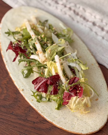 ервірування хрусткого салату з білого редису та радіккіо на світлій овальній керамічній тарілці, посипаного горіхами, CookItTwice стиль.