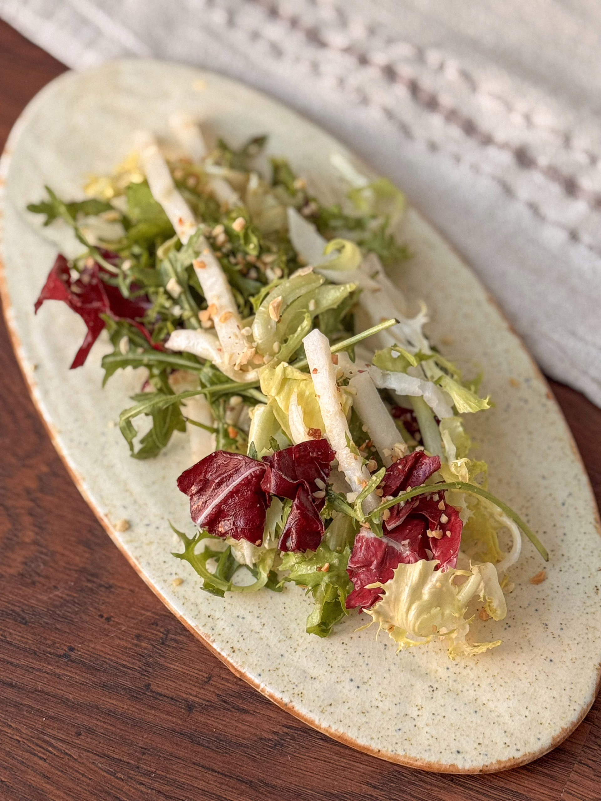 ервірування хрусткого салату з білого редису та радіккіо на світлій овальній керамічній тарілці, посипаного горіхами, CookItTwice стиль.