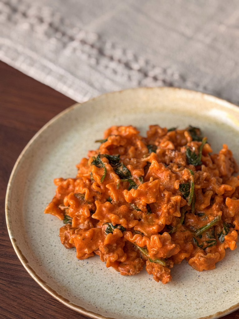 Сервірування гарячої пасти мафальда з м'ясним соусом та шпинатом у керамічній матовій тарілці, поруч вінтажна виделка, CookItTwice стиль.