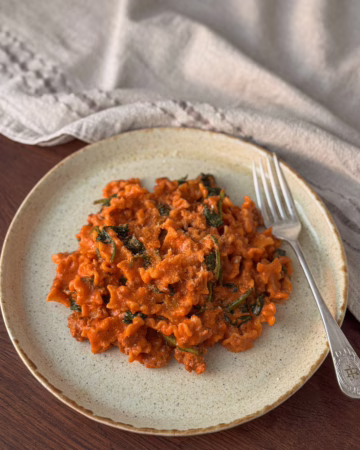 Сервірування гарячої пасти мафальда з м'ясним соусом та шпинатом у керамічній матовій тарілці, поруч вінтажна виделка, CookItTwice стиль.