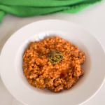 Сервірування гарячого птісото з м'ясом у білій глибокій керамічній тарілці, зверху ложка холодного песто, на фоні зелена лляна серветка, CookItTwice стиль.