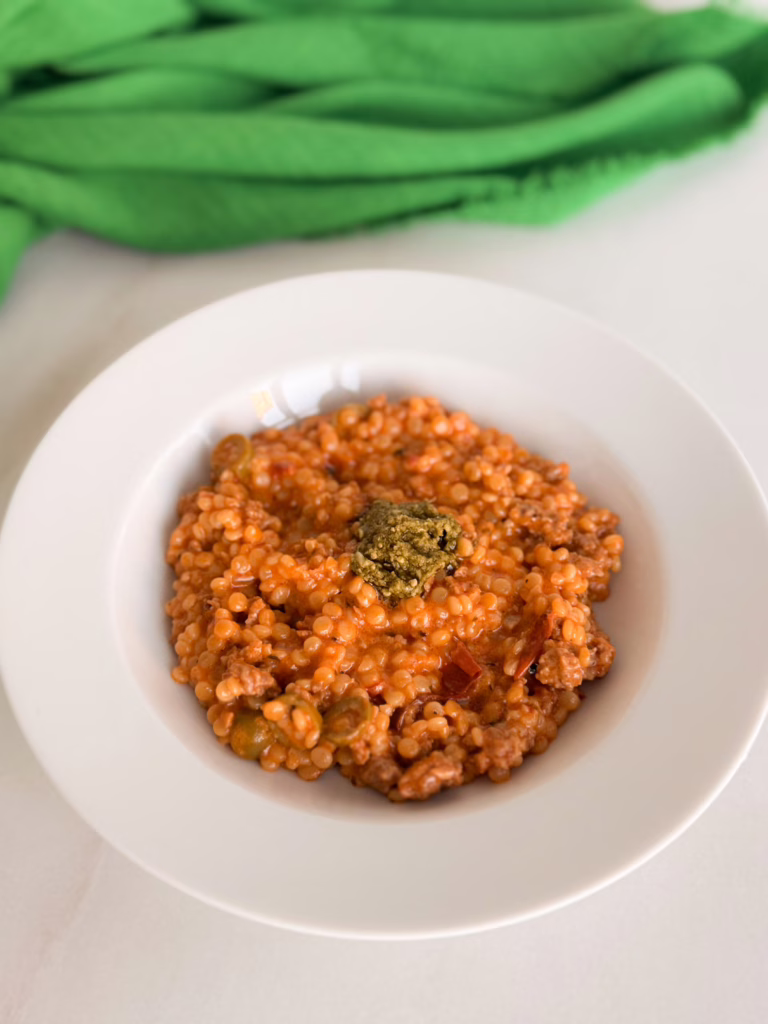 Сервірування гарячого птісото з м'ясом у білій глибокій керамічній тарілці, зверху ложка холодного песто, на фоні зелена лляна серветка, CookItTwice стиль.