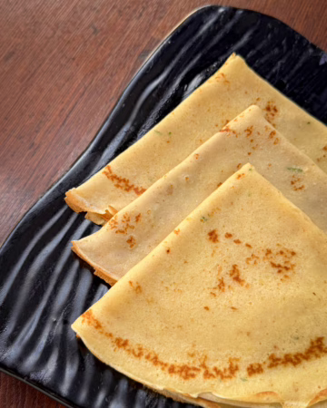 Тонкі золотисті данські млинці pandekager, складені стопкою на красивій тарілці, поруч стоїть баночка з ягідним варенням та чашка гарячої кави