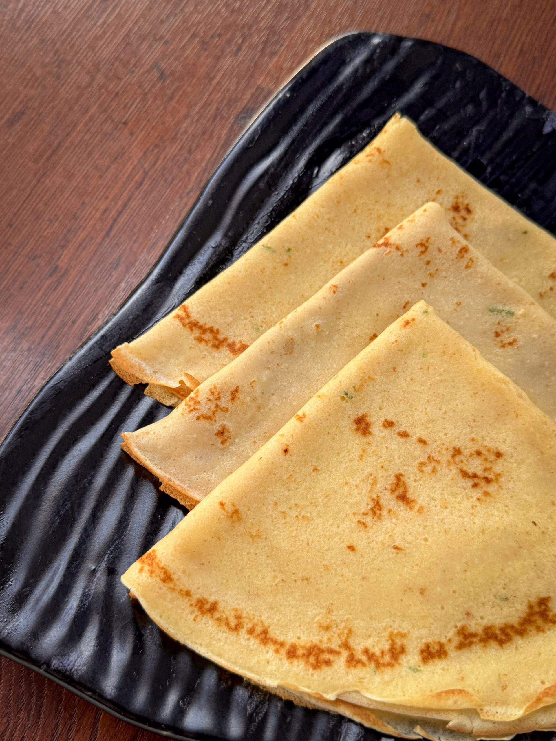 Тонкі золотисті данські млинці pandekager, складені стопкою на красивій тарілці, поруч стоїть баночка з ягідним варенням та чашка гарячої кави