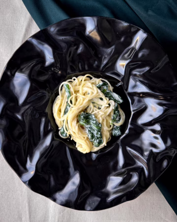 Сервірована на чорному блюді паста з лимоном та рікотою й шпинатом.