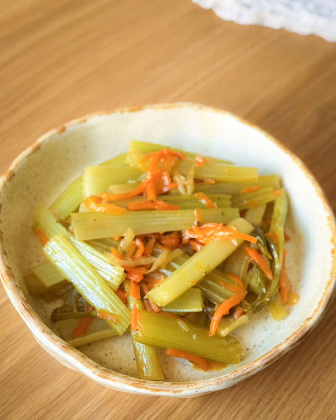 Томлена стеблова селера у глянцевій глазурі з морквою та цибулею у керамічній тарілці.