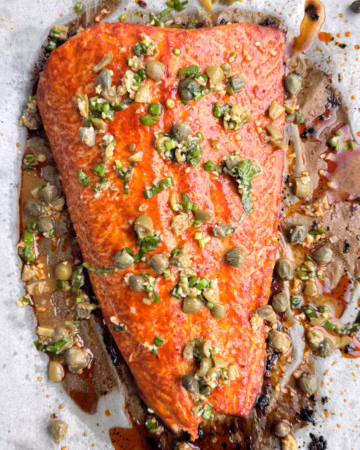 Запечене філе червоної риби на тарілці з зеленою сальсою. Соус із тахіні в піалі.