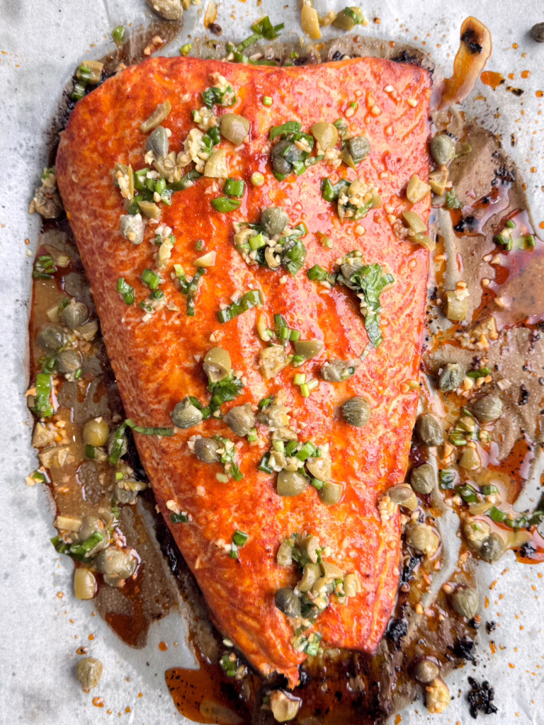 Запечене філе червоної риби на тарілці з зеленою сальсою. Соус із тахіні в піалі.