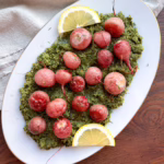 Блідо-рожева запечена редиска на подушці з текстурного зеленого песто, подана на порцеляновому блюді.