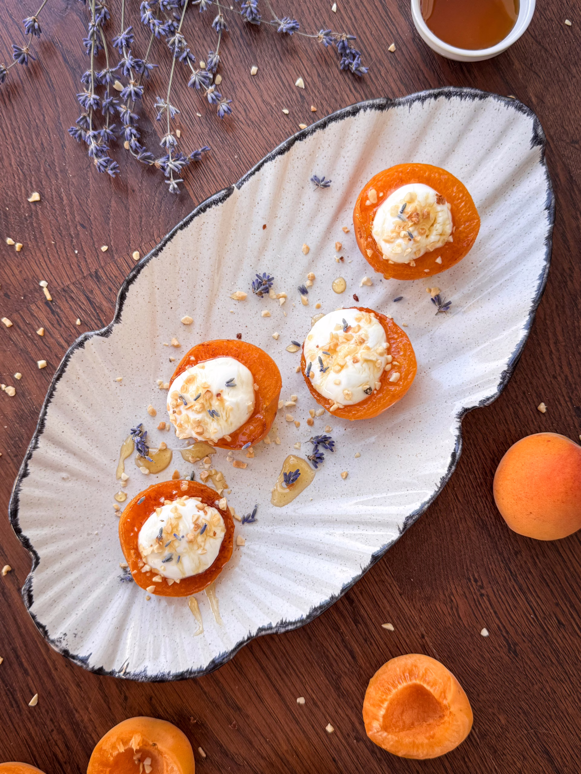 Теплі підсмажені половинки абрикосів з густим йогуртом, политі медом та посипані горіхами на світлій керамічній тарілці.